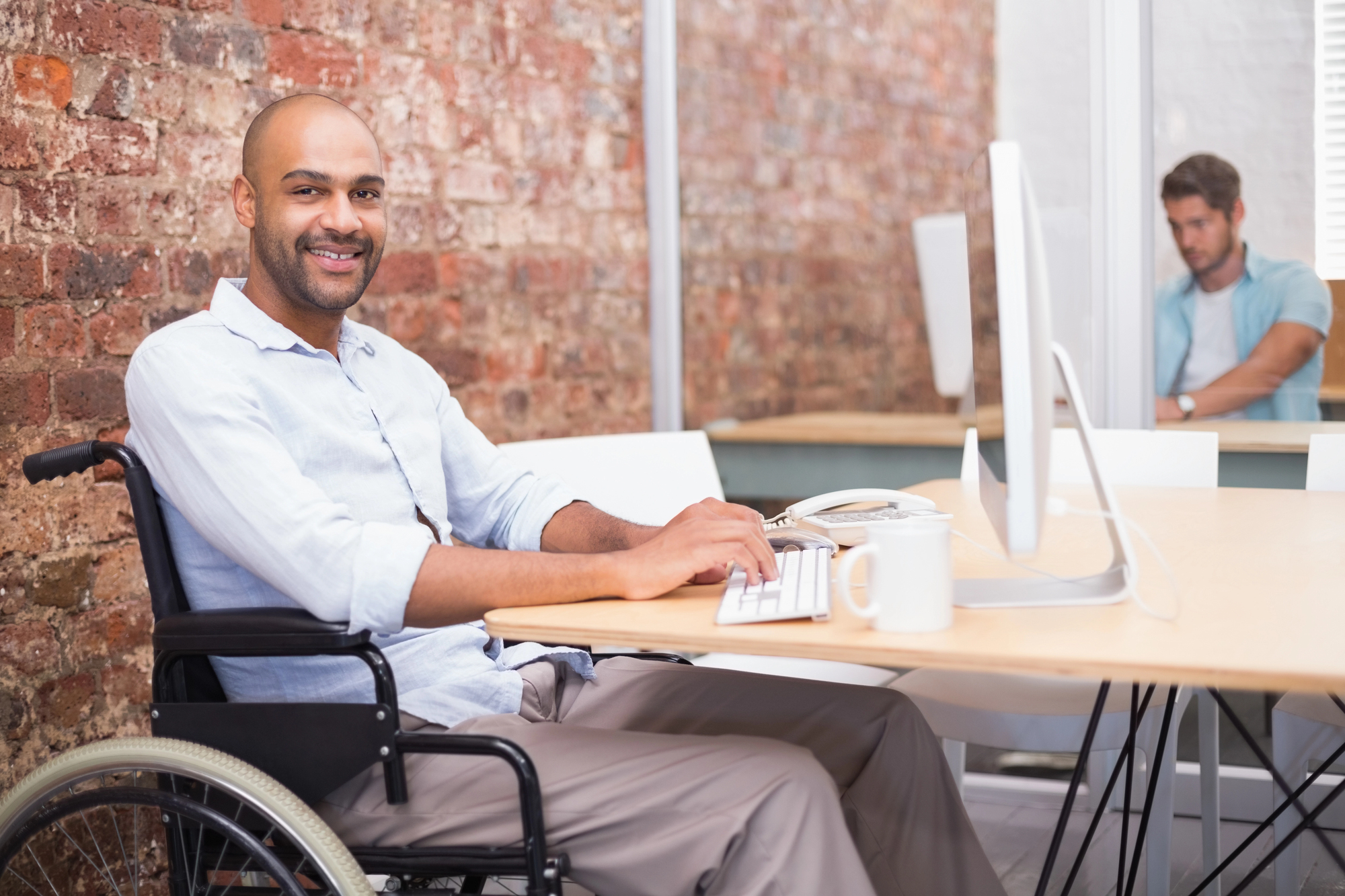 Person using a desktop computer in a wheelchair in an accessible office workspace.